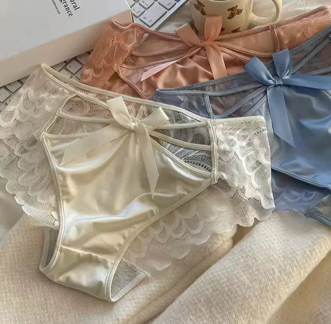 Elegant women’s lace panties with satin bows in ivory, peach, and blue, displayed for comfort and style.