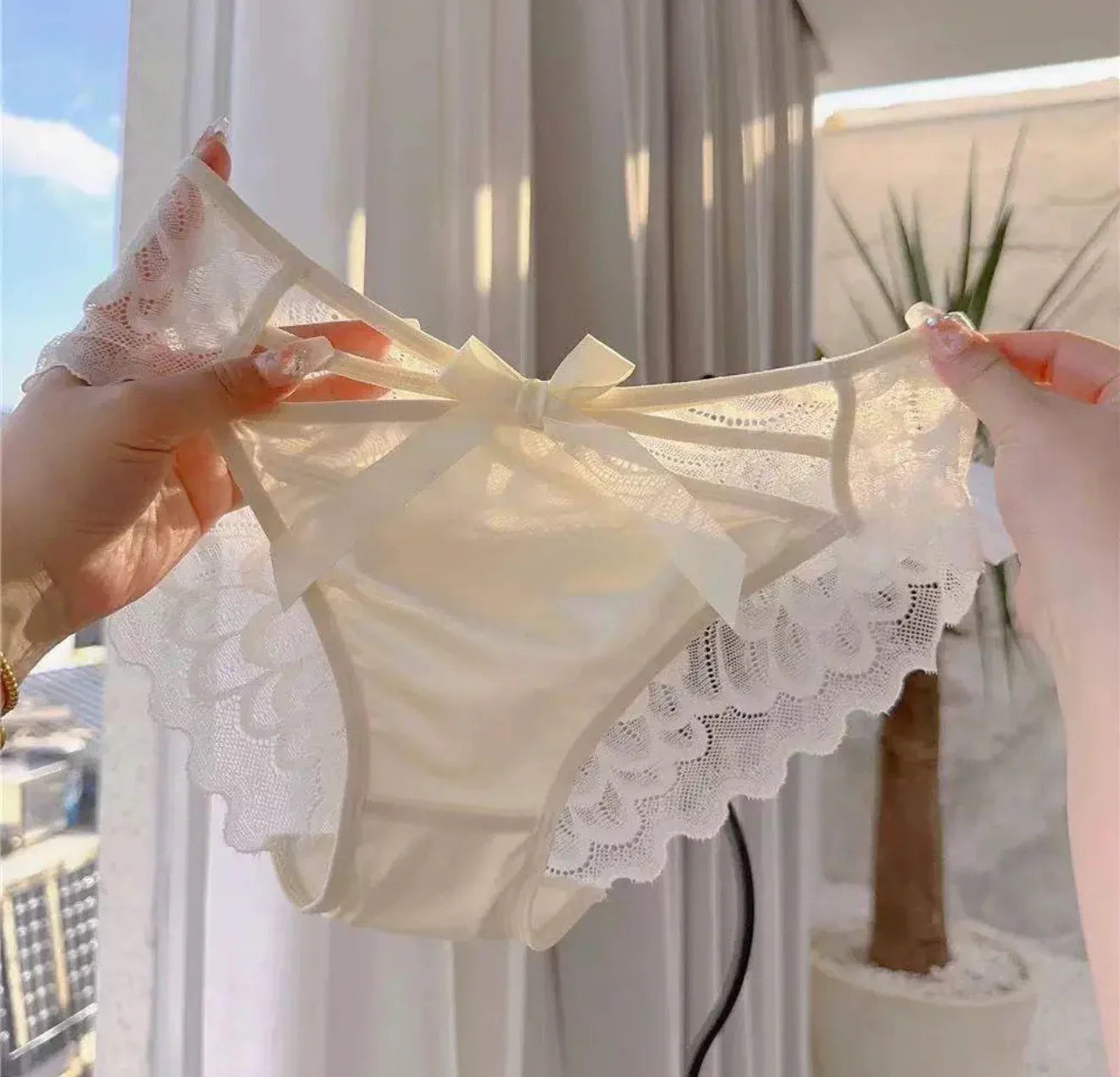 Hand holding soft cream lace panties with bow detail, women’s underwear for comfort and elegance